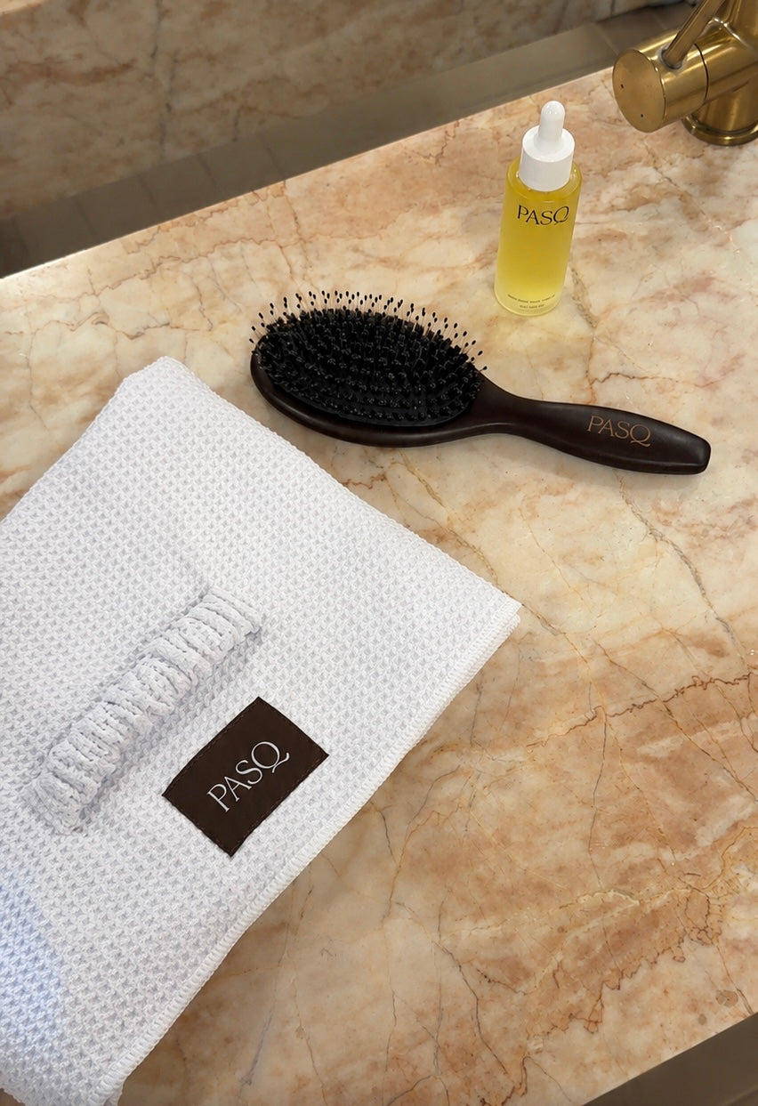 The PASQ Essentials Collection: hair oil, boar bristle brush and waffle hair towel on a marble vanity