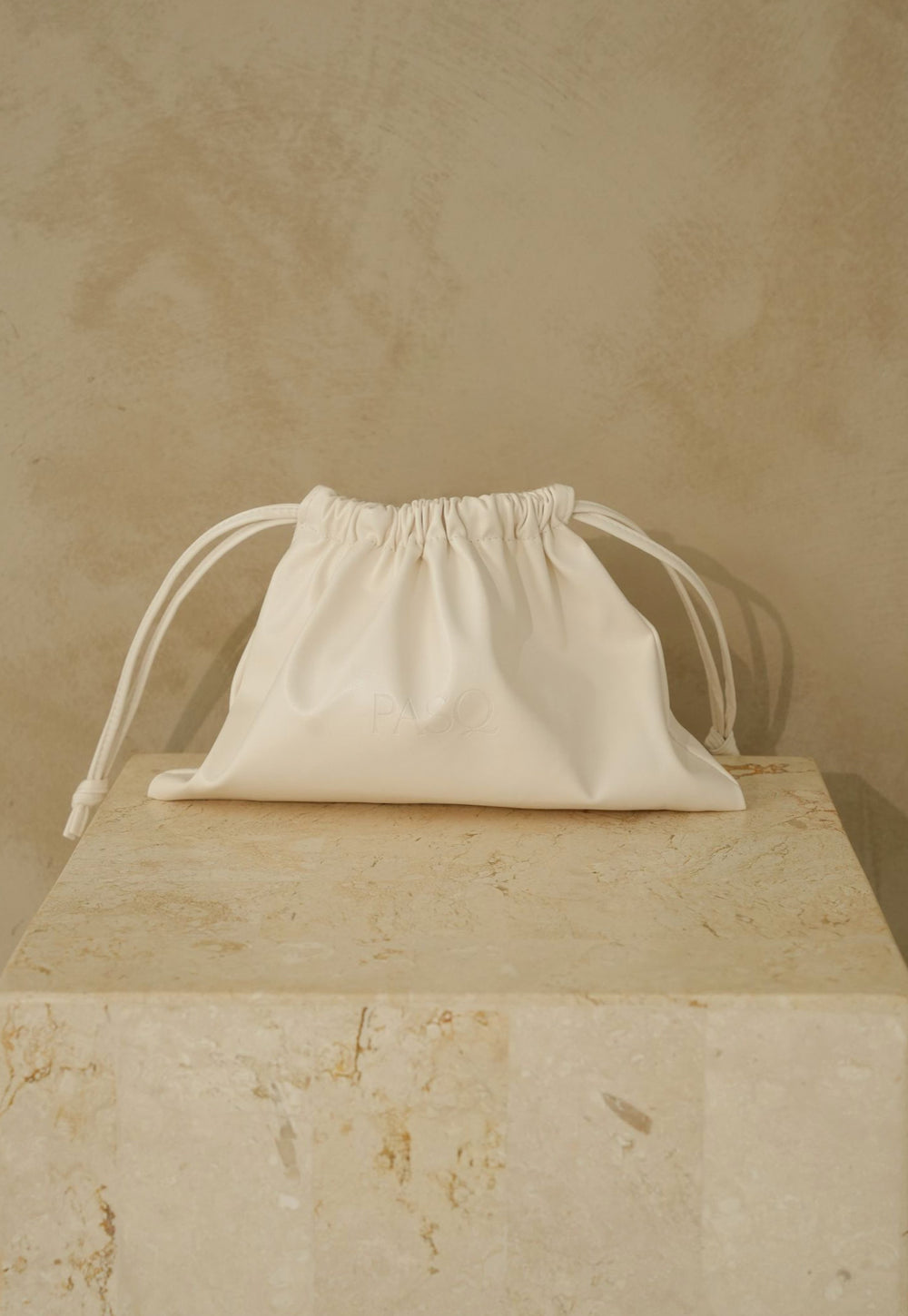 Cream leather PASQ Essentials Pouch with drawstring closure on a stone plinth