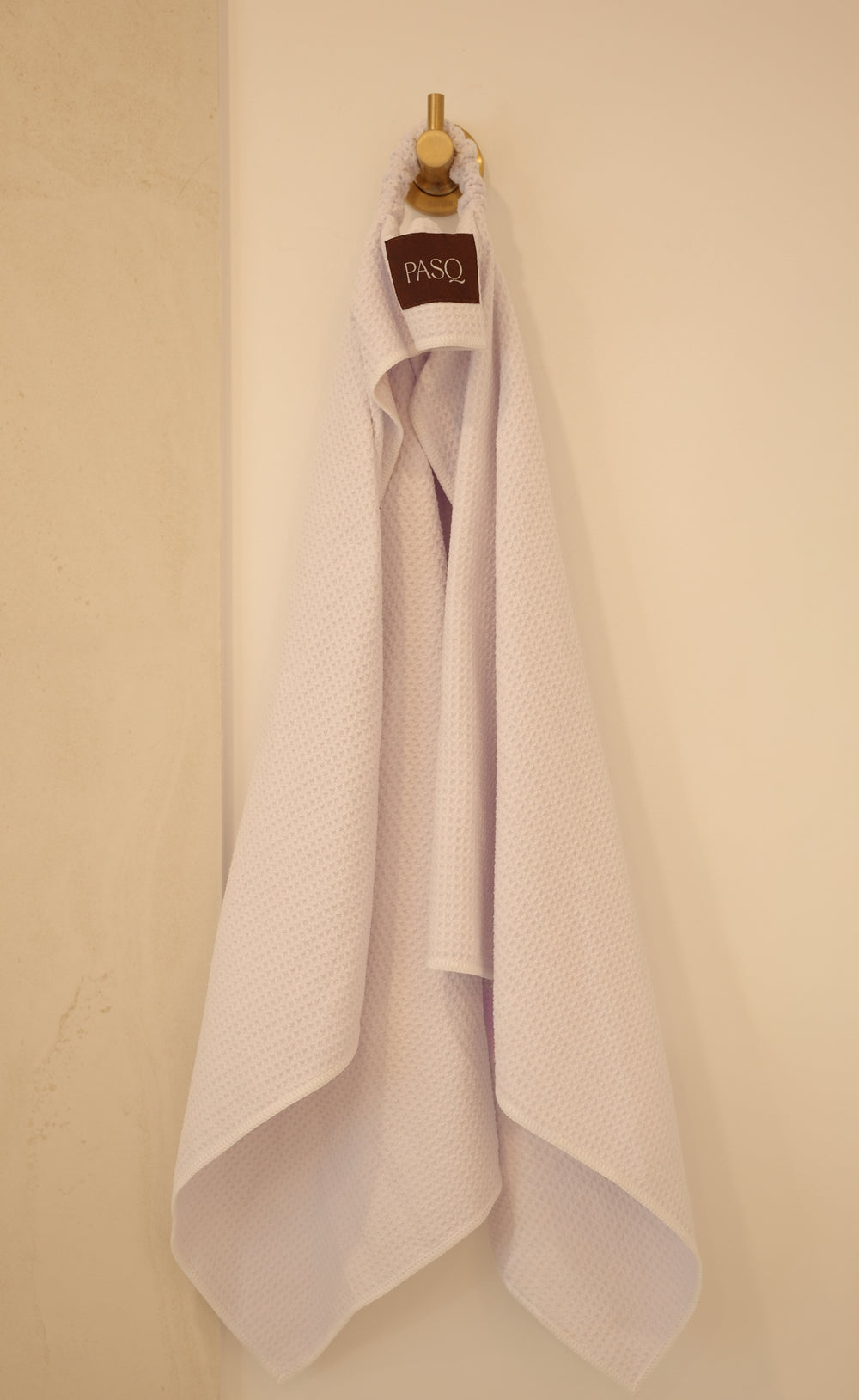 White waffle PASQ Hair Towel hanging from a wall hook by its loop