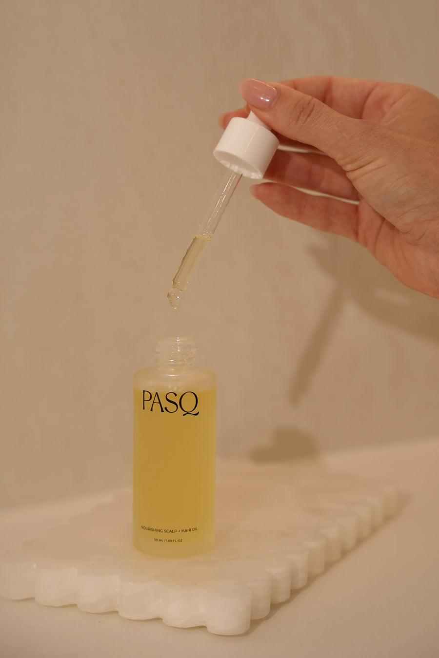 Hand dispensing PASQ scalp and hair oil from the glass dropper above the bottle